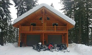 Eine Holzhütte mit einem Balkon, zwei Garagen und verschneiter Umgebung.