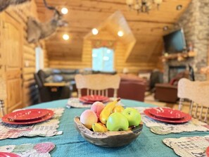 Ein rustikales Holzinterieur mit einem Esstisch, gedeckt für vier Personen, mit einer Obstschale und roten Tellern.