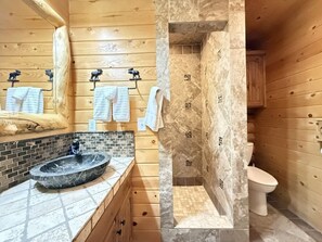 Ein Badezimmer mit Marmorwaschbecken, Holzwänden und einer gefliesten Duschkabine.