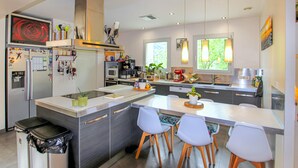 Een moderne keuken met een centraal eiland, witte stoelen en een zwarte prullenbak.