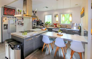Une cuisine moderne avec un îlot central, des chaises blanches et une poubelle noire.