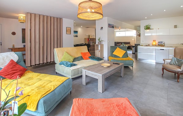 A modern living room with a sofa, coffee table, and chairs, a kitchen area, and a dining table.
