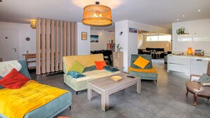 Een moderne woonkamer met een bank, fauteuil, salontafel en een eethoek, met een keuken op de achtergrond.