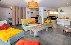 Un salon moderne avec un canapé, un fauteuil, une table basse et un coin repas, la cuisine étant visible à l’arrière-plan.