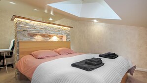 Een slaapkamer met een stenen accentmuur, een bed met roze en witte beddengoed, en een dakraam.