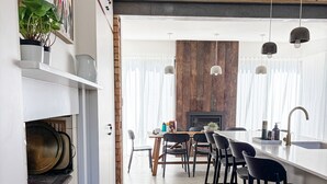 A modern kitchen with a brick wall, wooden flooring, and a dining area with bar stools. - Kent House | Luxury heritage home, Prime location (Albany)