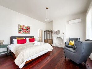 A bedroom with a bed, a chair, a fireplace, and a painting.