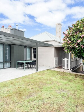 A modern house with a covered patio, a dining area, and a white fence.