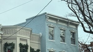 Un edificio de dos plantas con fachada azul claro, varias ventanas y una entrada principal con puerta.