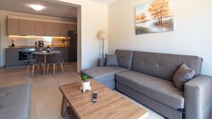 A modern living room with a grey sofa, a wooden coffee table, and a dining area with a table and chairs. - Vakakis Family Luxury Studios (Kantanos-Selino)