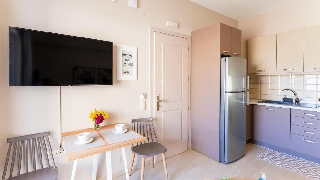 Cocina funcional con refrigerador, una mesa de comedor con sillas, un televisor de pantalla plana montado en la pared y un ventanal.