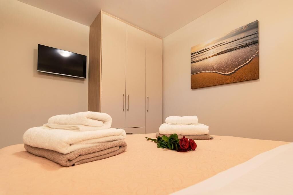 Habitación de hotel con cama, televisor montado en la pared, un cuadro de playa y toallas sobre la cama.