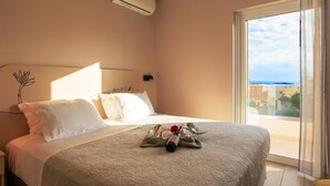 A hotel room with a bed, a nightstand, a window with a view, and an air conditioning unit. - Vakakis Family Luxury Studios (Kantanos-Selino)