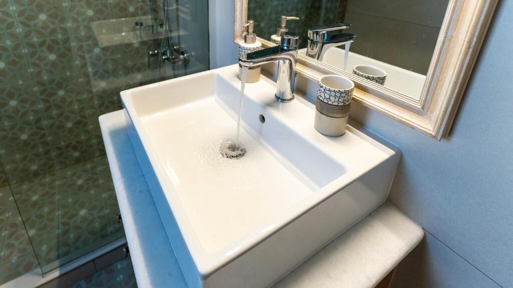 A bathroom with a white sink, a faucet, and a cup.
