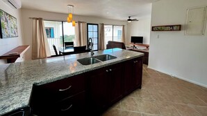 Una cocina con encimera de granito, un fregadero, un ventilador de techo y una zona de comedor con mesa y sillas.
