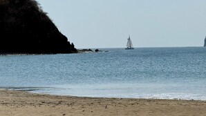 Una playa con un velero en el agua, un acantilado rocoso y un cielo despejado.