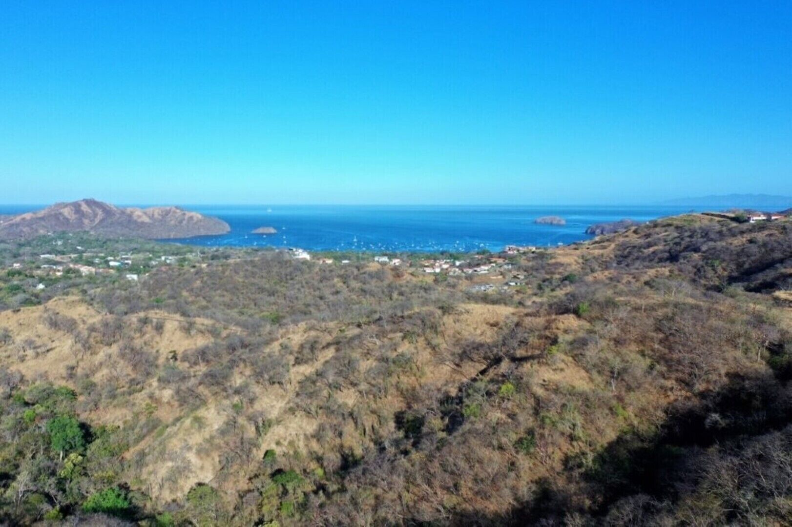 A mountainous landscape with a small settlement and a clear view of the ocean.