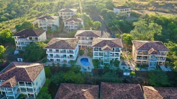 Un conjunto de edificios de varios pisos con una piscina central, rodeado de abundante vegetación.