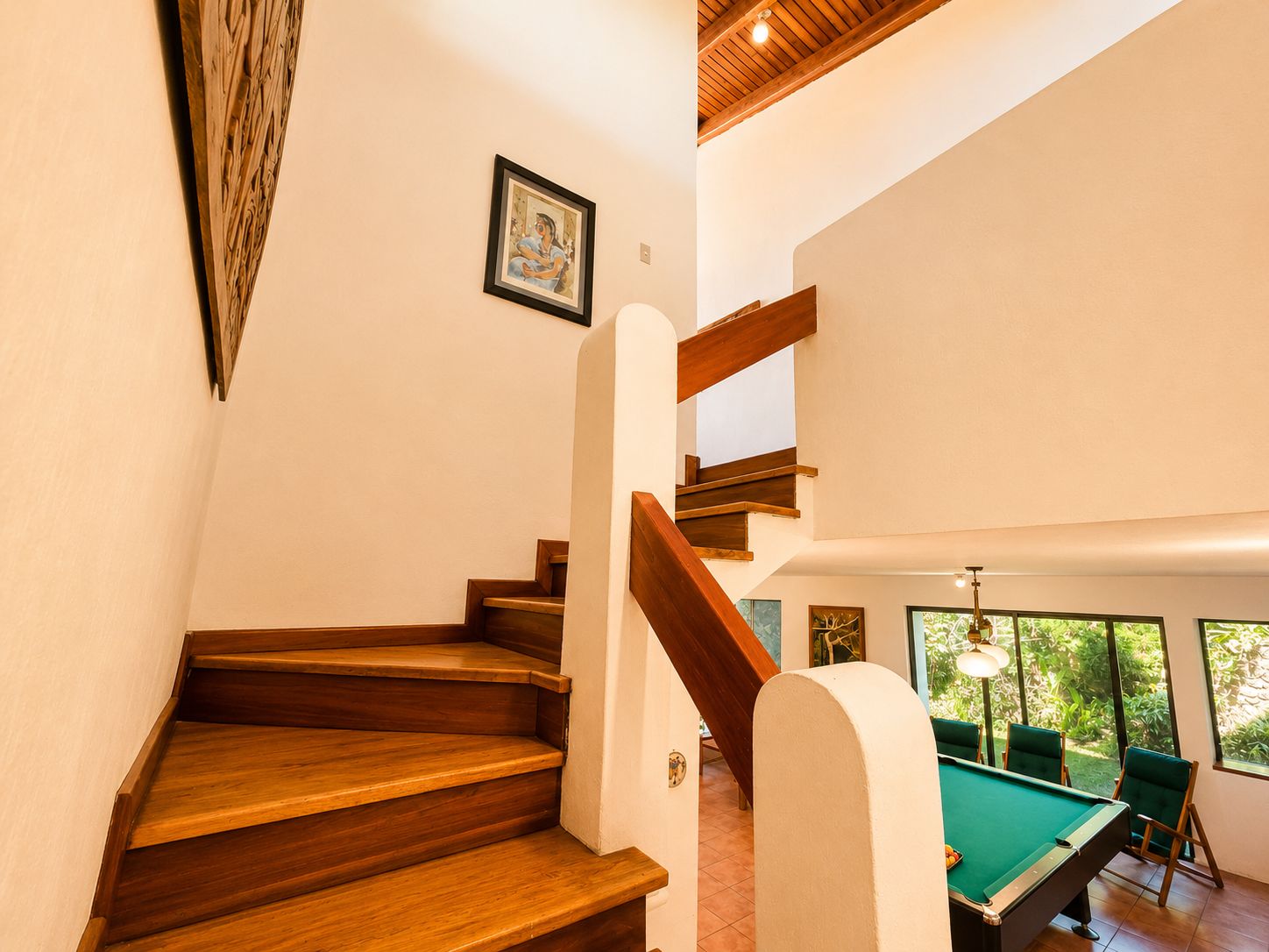 Una escalera de madera que conduce a una habitación con una mesa de billar y sillas verdes.