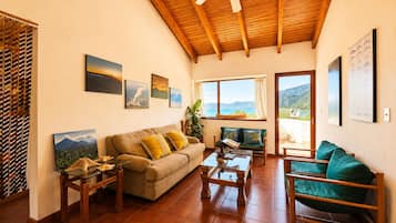 A spacious living room with a wooden ceiling, a sofa, a coffee table, and a view of the sea through large windows.