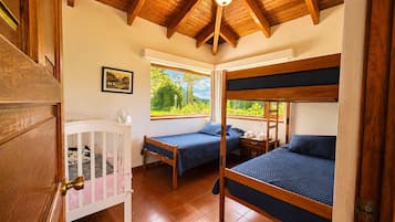 A room with a high wooden ceiling, two bunk beds, a crib, and a window with a view of greenery.