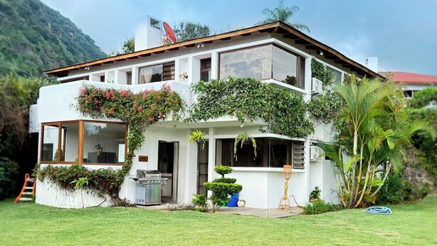 Una casa de dos pisos con fachada blanca, ventanas grandes y una antena parabólica.