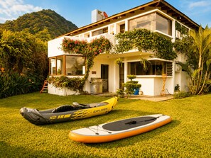 Ein modernes Haus mit gepflegtem Rasen, einem Kajak und einem Stand-Up-Paddleboard.