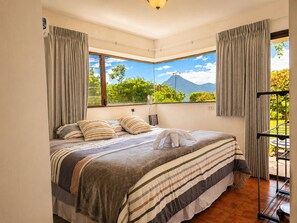 A bedroom with a bed, curtains, a window with a mountain view, and a balcony with a railing.