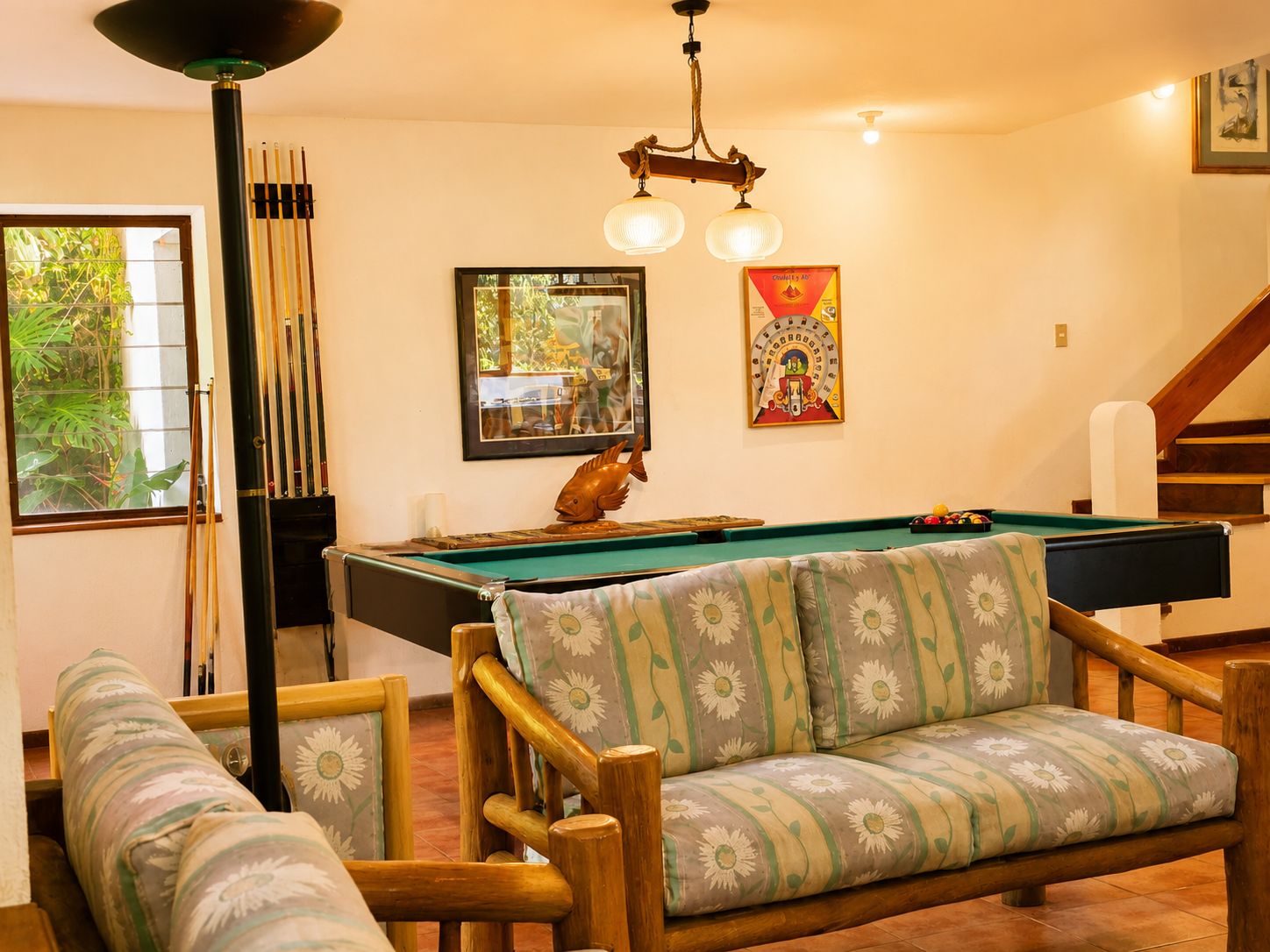 Una sala de billar con mesa de pool, muebles de madera y una escalera.