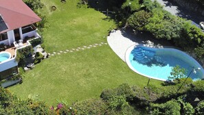 Una propiedad residencial con piscina, una casa de techo rojo y un césped cuidado.