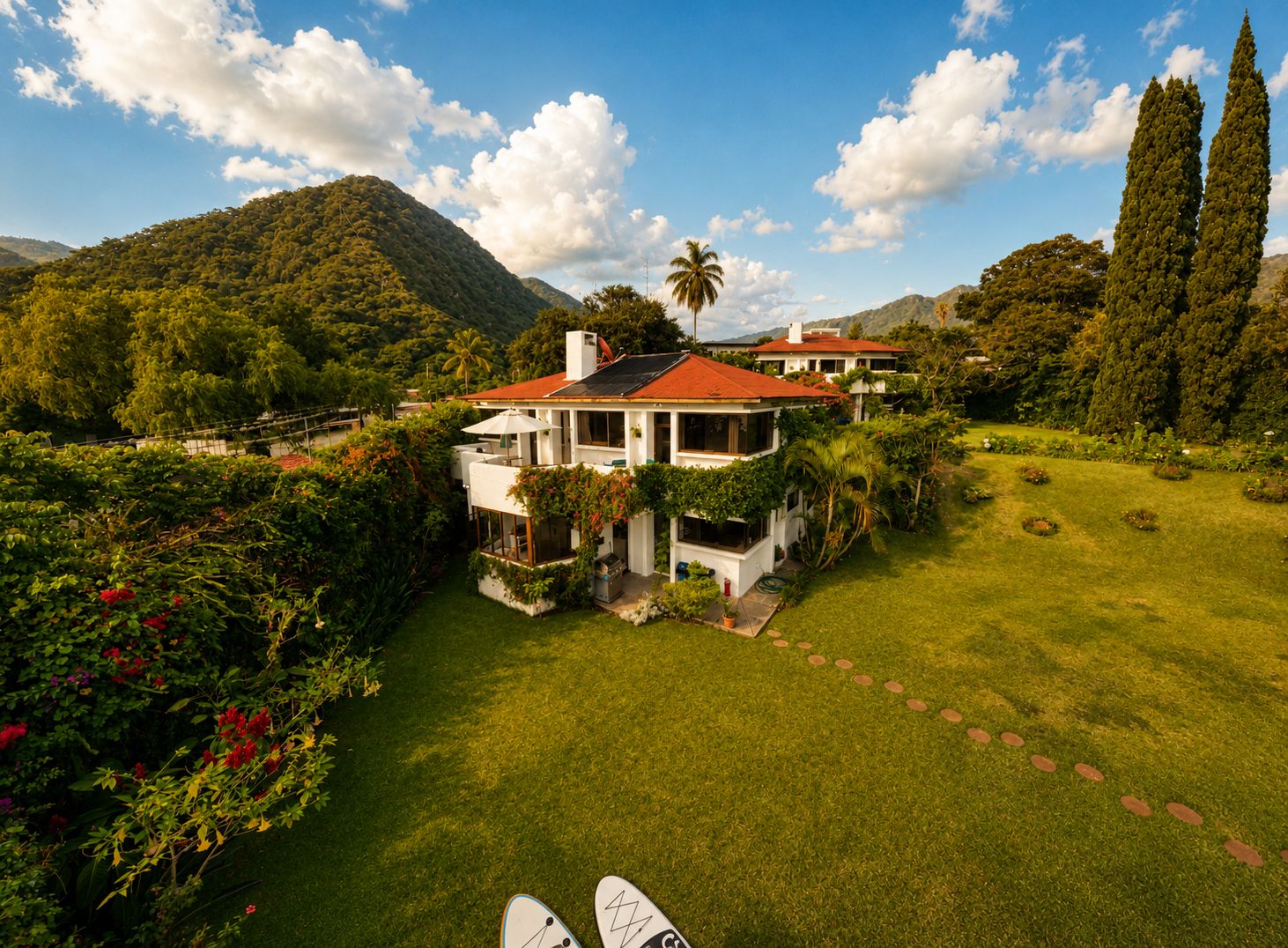 A house with a red roof, surrounded by lush greenery and mountains.