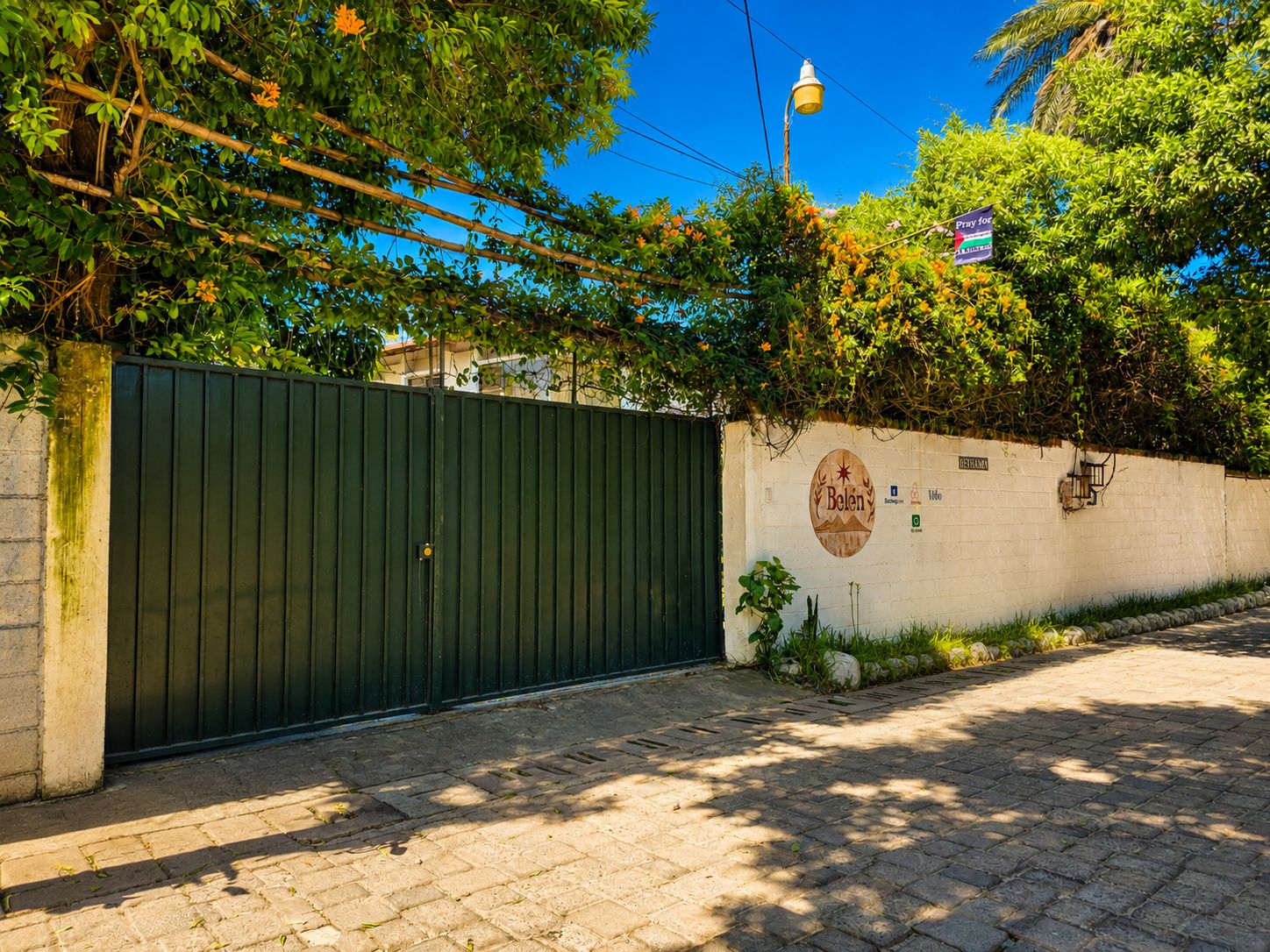 A gated entrance with a wall-mounted sign, a street lamp, and a paved pathway.
