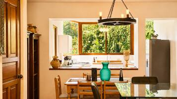 A dining area with a wooden table, chairs, a window with a view of greenery, and a hanging light fixture.