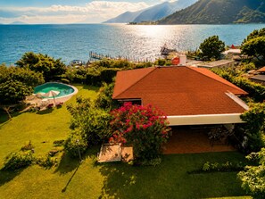 A residential property with a swimming pool, a red-roofed house, and a view of a lake and mountains.