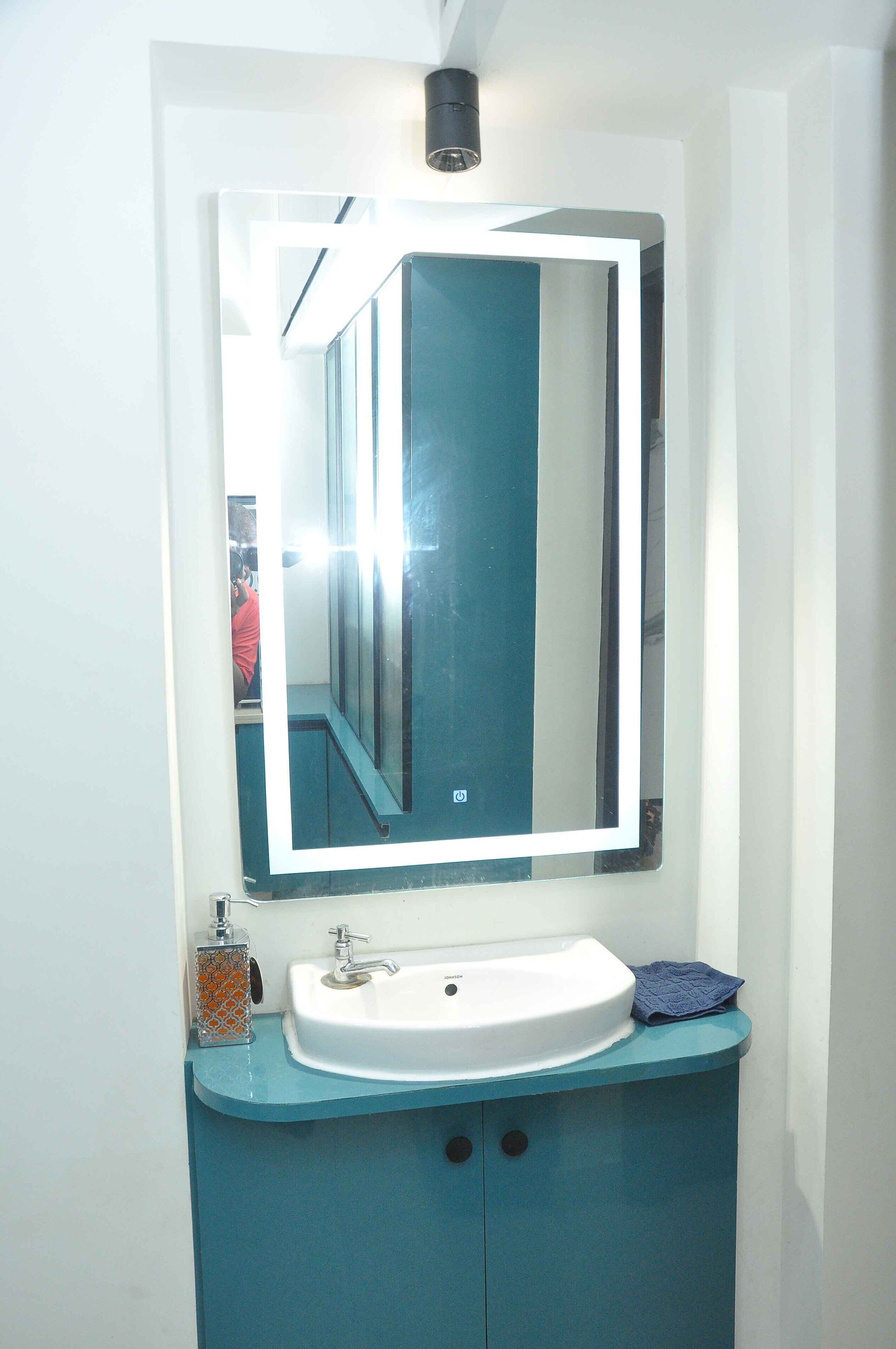 Een badkamer met een wit wastafel, een blauwe kast en een spiegel met verlichting erboven.