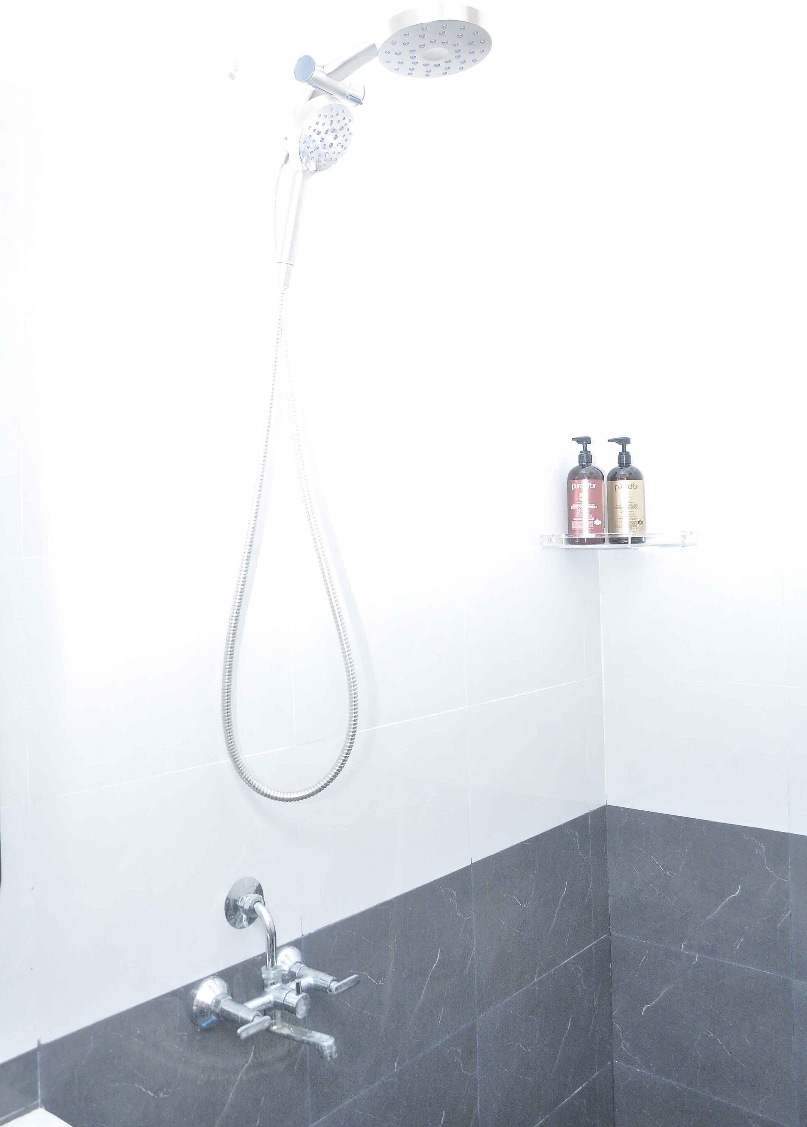 Ducha con cabezal de ducha manual y grifo empotrado. Hay dos botellas en un estante.