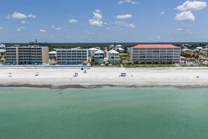 Ein Strandhotel mit mehreren Gebäuden, einem Sandstrand und klarem türkisblauem Wasser.