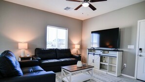 A living room with a black leather sofa, a coffee table, a flat-screen TV, and a ceiling fan. - Southwest Tucson Corner Retreat "Close to Great food and Shopping" (Tucson)