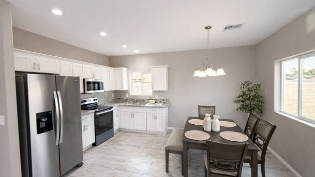 A modern kitchen with stainless steel appliances, white cabinets, a granite countertop, and a dining area with a table and chairs. - Southwest Tucson Corner Retreat "Close to Great food and Shopping" (Tucson)