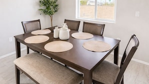 A dining area with a dark wooden table, six chairs, and a bench. There are placemats on the table, a potted plant, and a window with a view of the outdoors. - Southwest Tucson Corner Retreat "Close to Great food and Shopping" (Tucson)