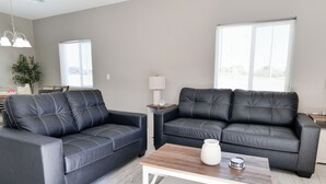 A modern living room with two black leather sofas, a wooden coffee table, a small side table with a lamp, and a large window providing natural light. - Southwest Tucson Corner Retreat "Close to Great food and Shopping" (Tucson)
