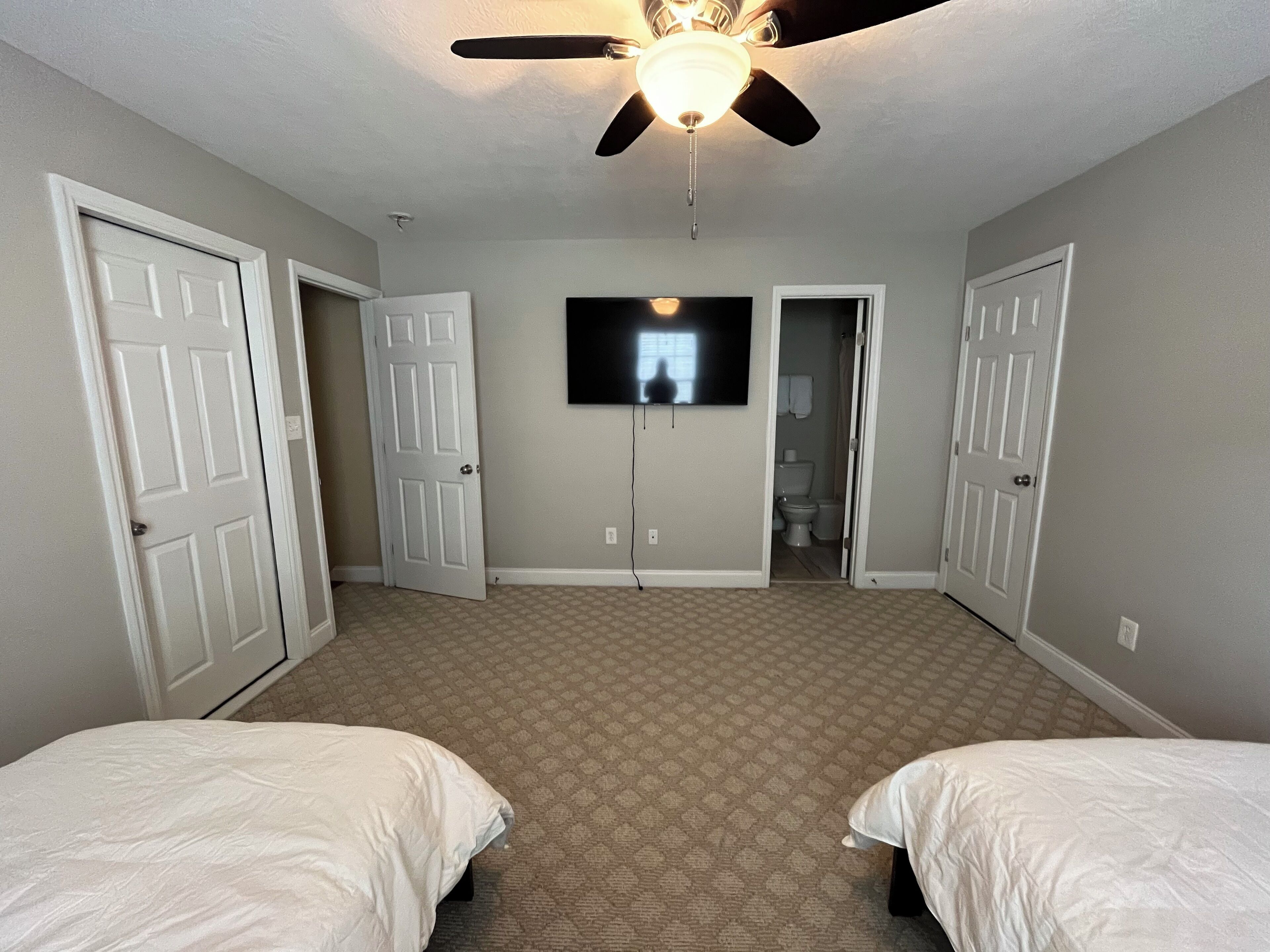 A bedroom with two beds, a ceiling fan, a TV, and a bathroom door.