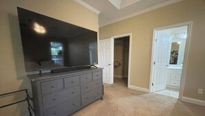 Ein Zimmer mit einem großen Flachbildfernseher an der Wand, einer grauen Kommode mit mehreren Schubladen und einem begehbaren Kleiderschrank mit Tür zum Badezimmer.
