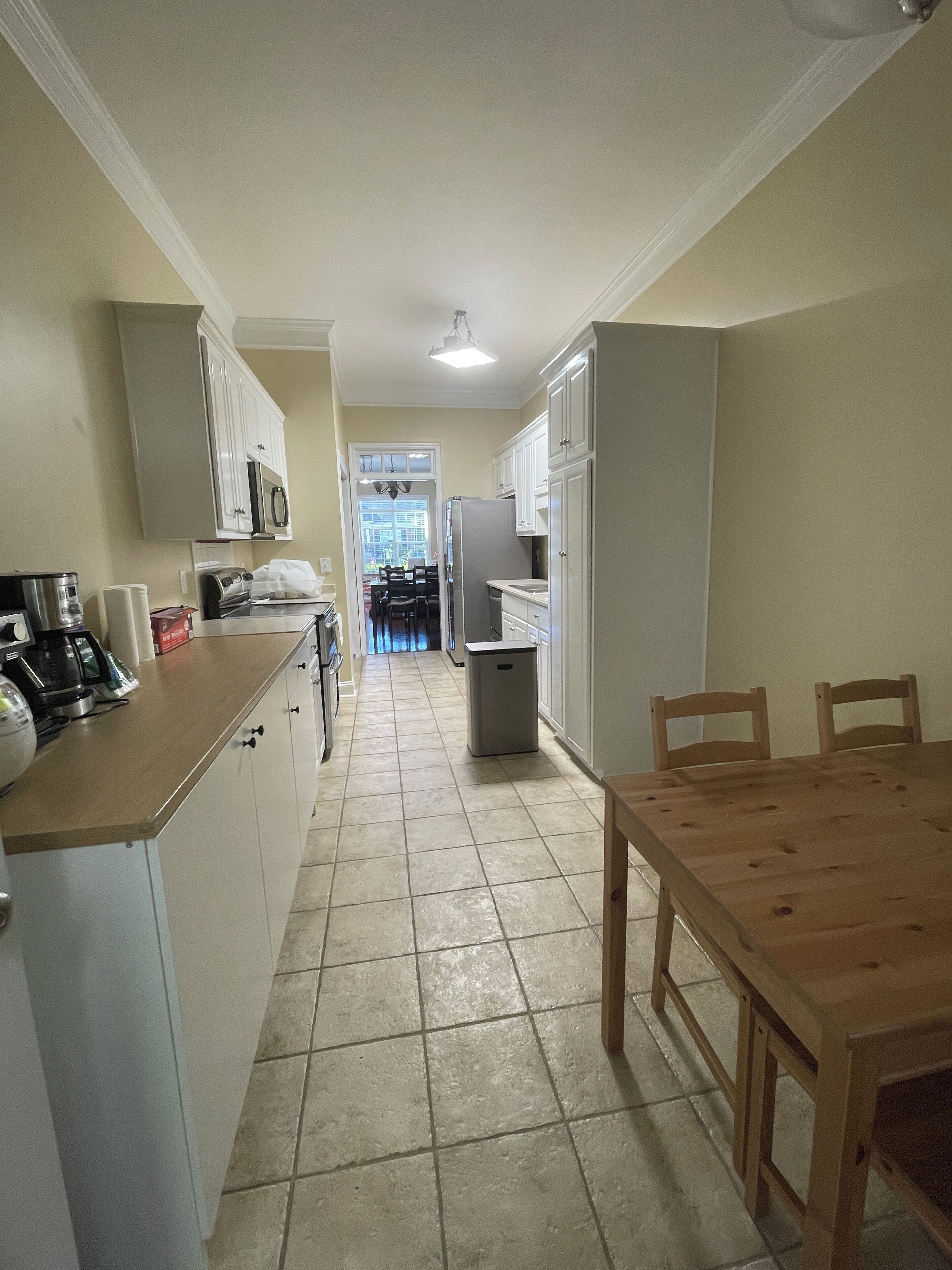 A compact kitchen with white cabinets, a wooden dining table, and a view into the dining area.