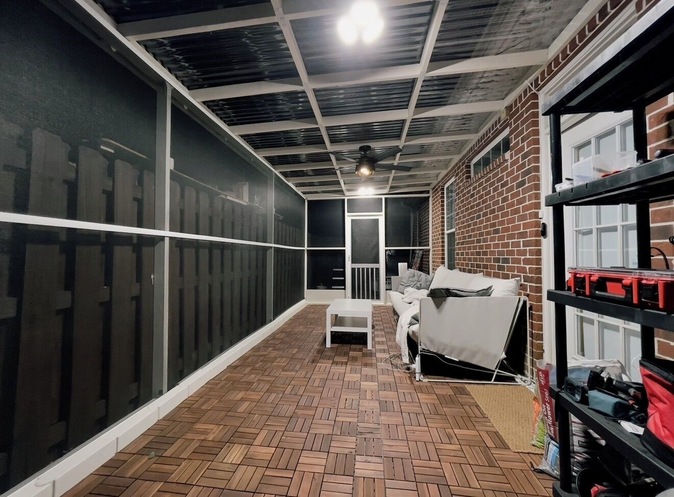 Une pièce dotée d’un parquet en bois à motifs chevrons, d’un canapé blanc, d’une table basse blanche, d’un mur en briques et d’un plafond avec des poutres apparentes et un luminaire.