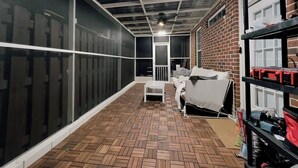 Ein Zimmer mit Fischgrätparkettboden, einem weißen Sofa, einem weißen Couchtisch, einer Ziegelwand und einer Decke mit freiliegenden Balken und einer Leuchte.