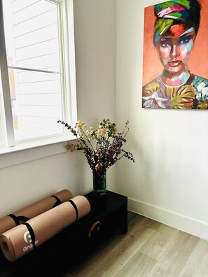 A room with a window, a painting on the wall, a vase with flowers, and yoga mats on a black table. - Modern 3BR, Private Backyard, Minutes to Downtown (Houston)