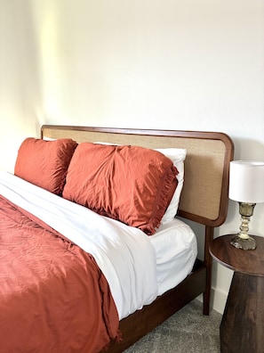 A neatly made bed with a wooden headboard, a white and red bedspread, and a small bedside table with a lamp. - Modern 3BR, Private Backyard, Minutes to Downtown (Houston)