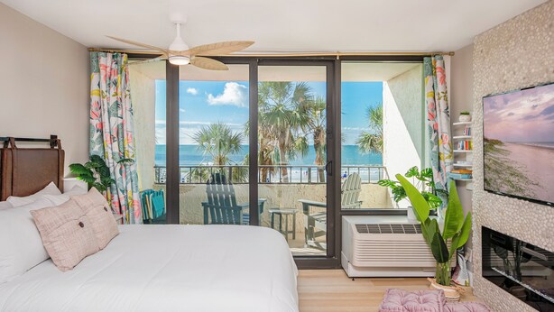 Une chambre dotée d’un grand lit, d’un ventilateur de plafond, d’un balcon avec vue sur l’océan et d’un téléviseur fixé au mur.