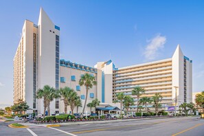 A modern hotel with multiple floors, a flat roof, and a parking area with cars and palm trees. - New Reno@Ocean Reef: 2nd floor OceanFront w/ full kitchen (Myrtle Beach)